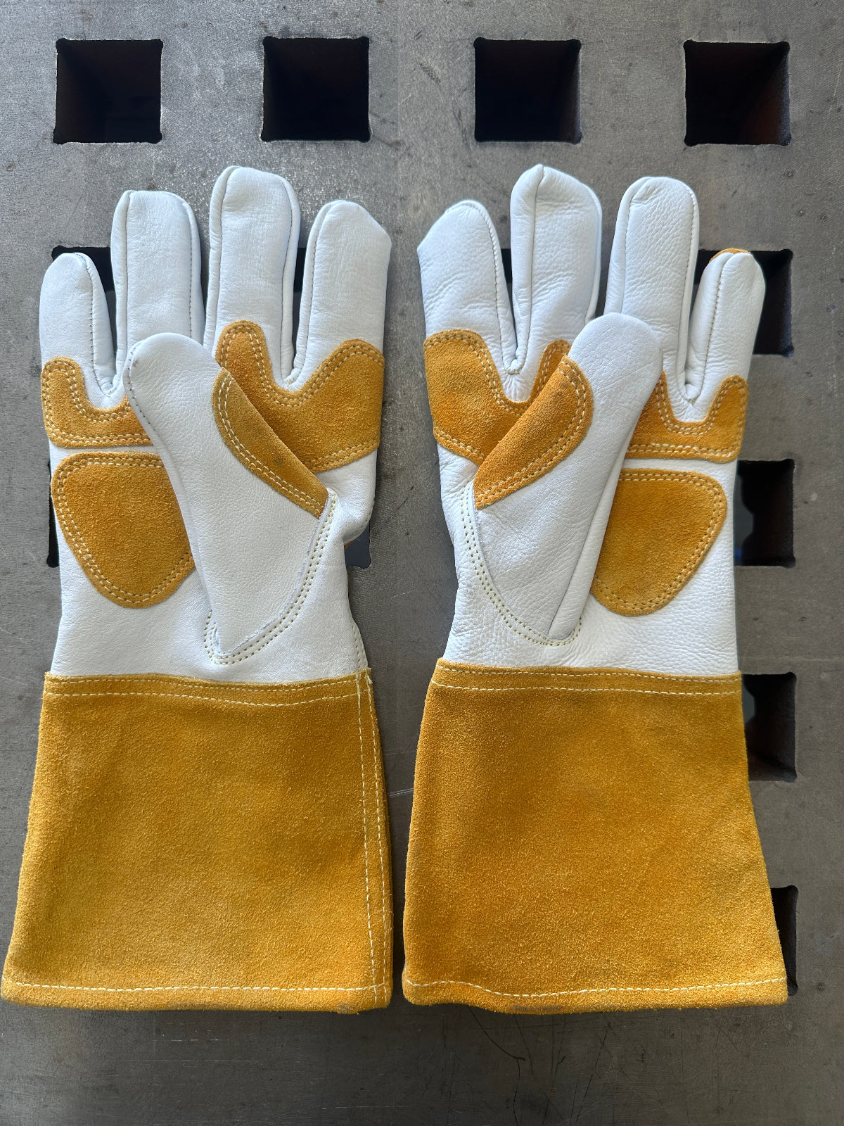 Pair of white and light brown gloves on a gray surface with black squares.