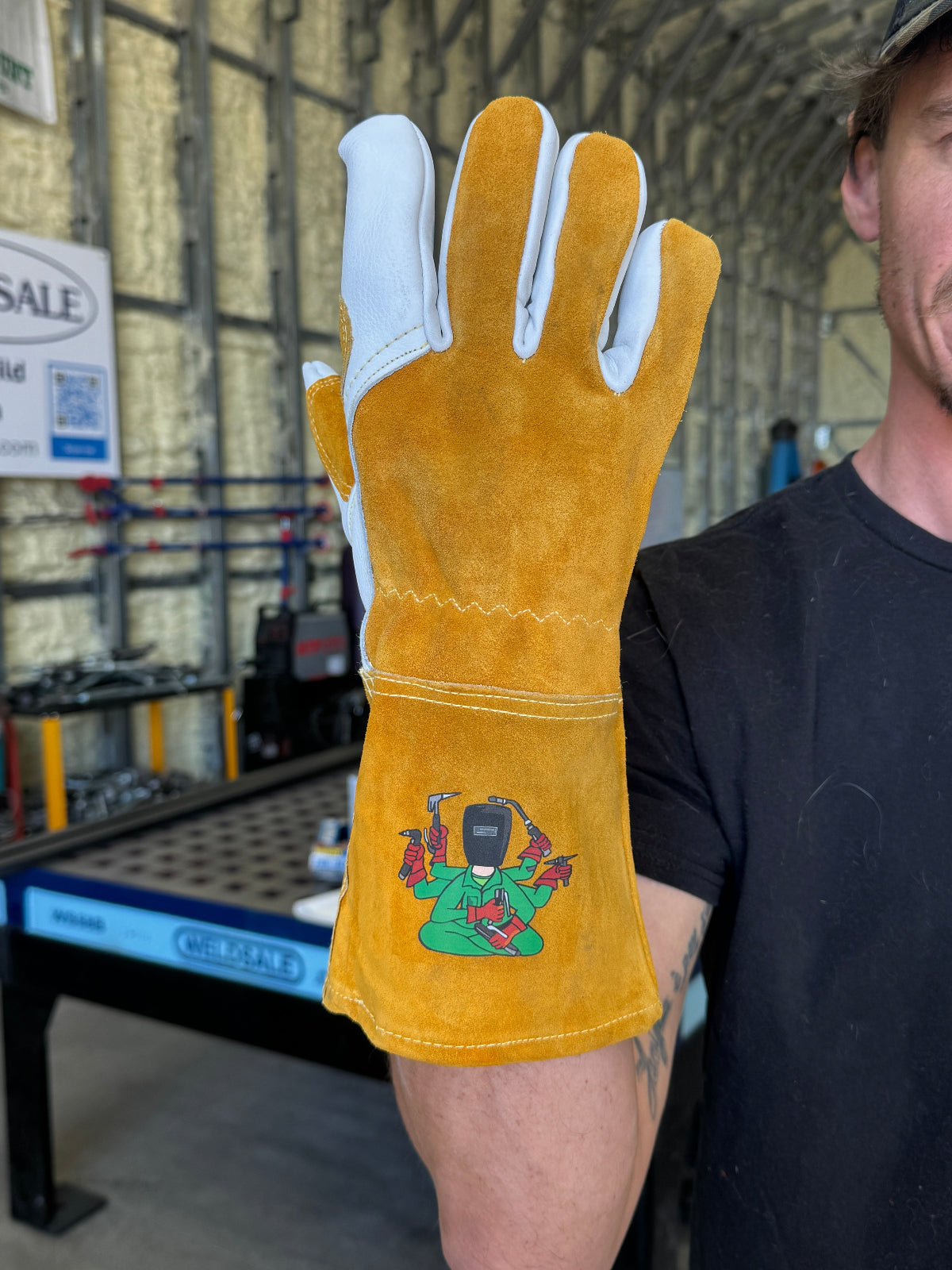 Person wearing a ylight brown welding glove with a design on it, in an industrial setting.