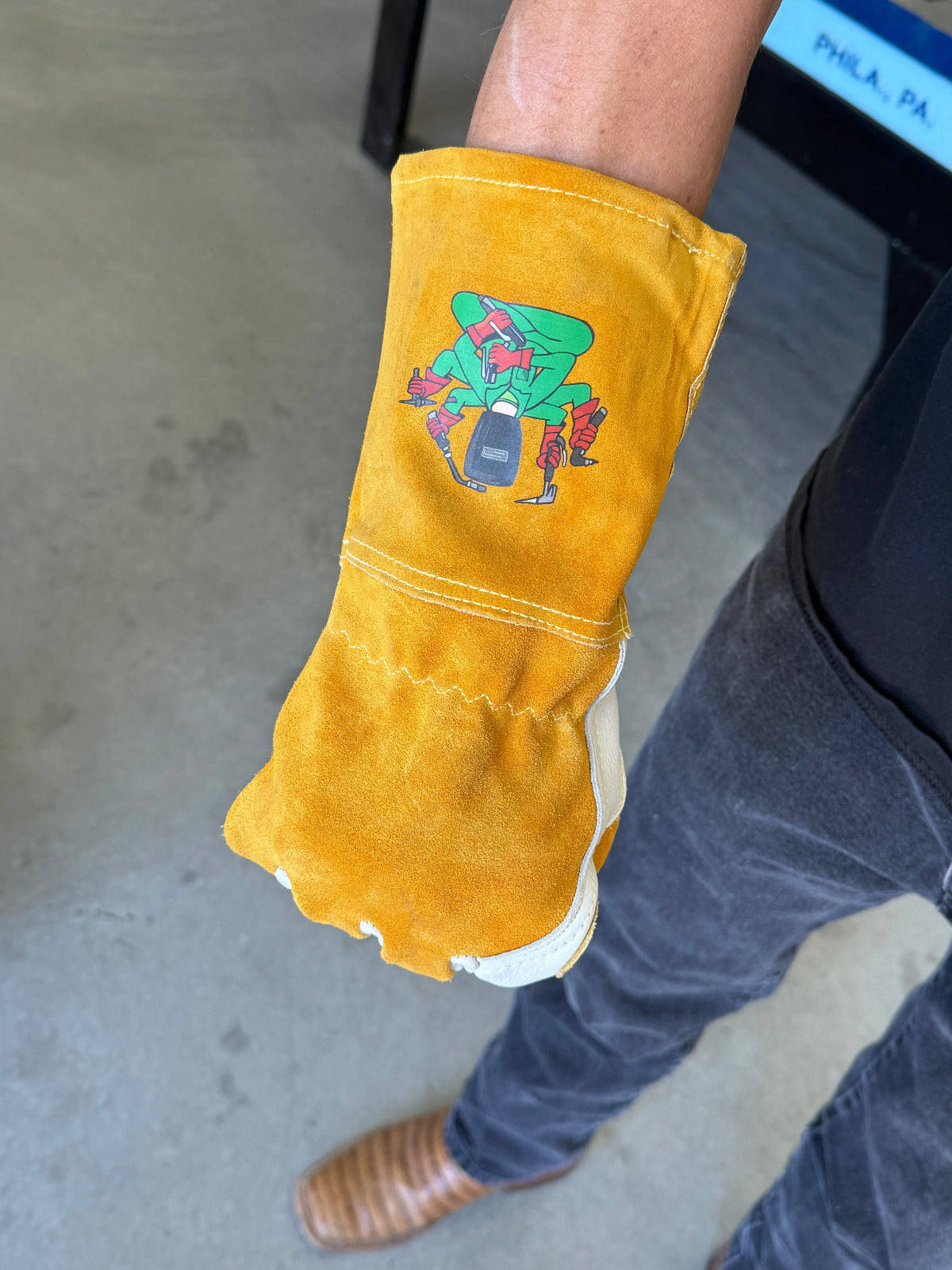Light Brown glove with a colorful design on a person's hand, wearing jeans and brown shoes.